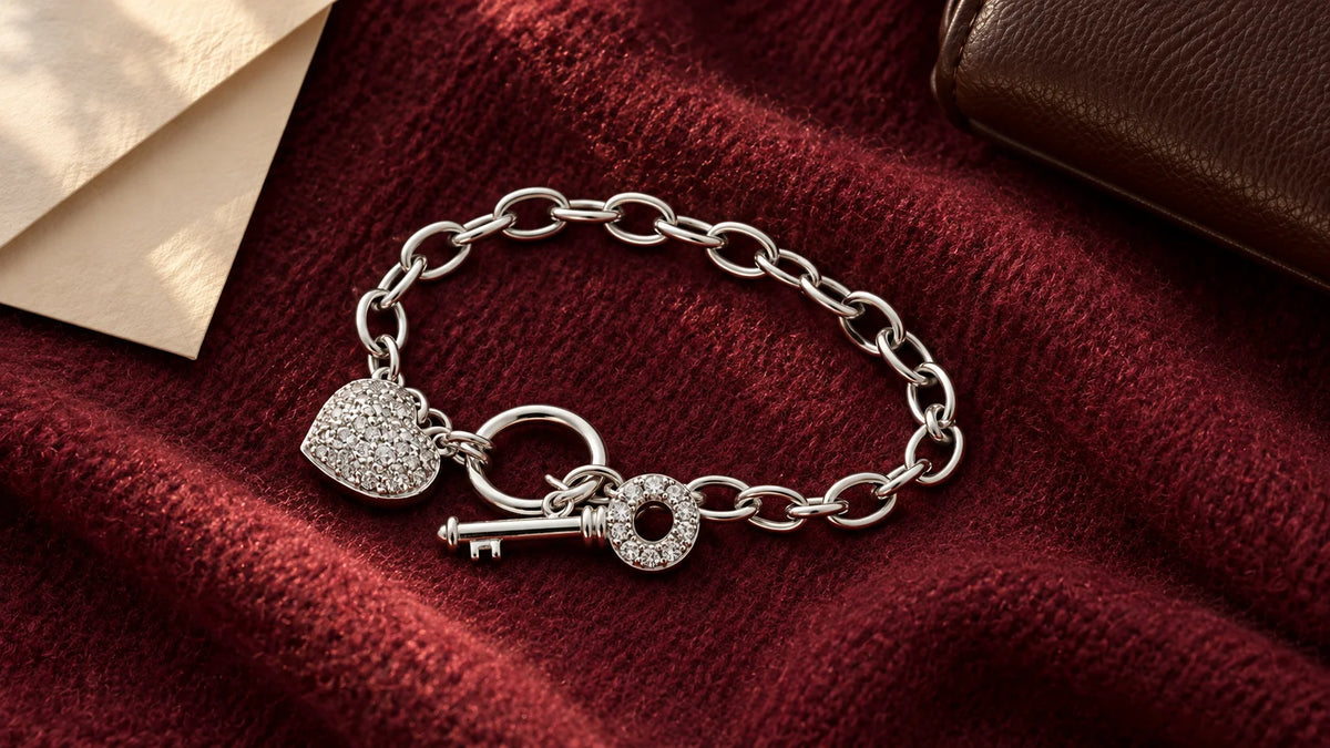 Silver-tone heart and key charm bracelet arranged on burgundy wool in an editorial overhead flat lay.