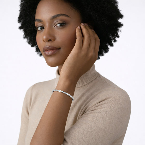 Close-on-model view of a silver tone channel-set crystal cuff resting over a beige sweater sleeve, adding a subtle line of sparkle against warm brown skin.