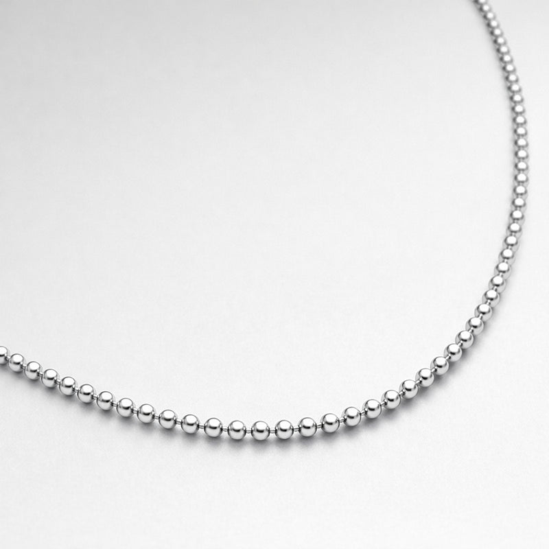 Close up studio image showing the polished round beads of a silver tone beaded chain necklace.
