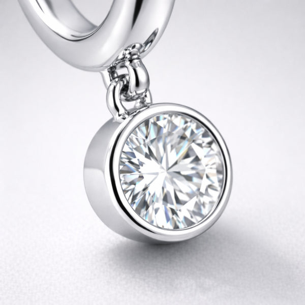 Detail view of the dangling cubic zirconia charm in a smooth bezel style setting attached to a silver tone hoop.