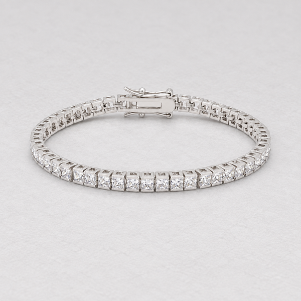 Full oval silver-tone bracelet with clear square stones on a pale textured surface.