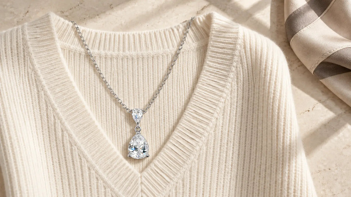 Pear-shaped silver-tone pendant arranged on a cream V-neck sweater