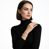 Studio shot shows a slim silver tone cuff edged with clear channel-set crystals on a model in a black ribbed turtleneck, highlighting sleek wrist sparkle.