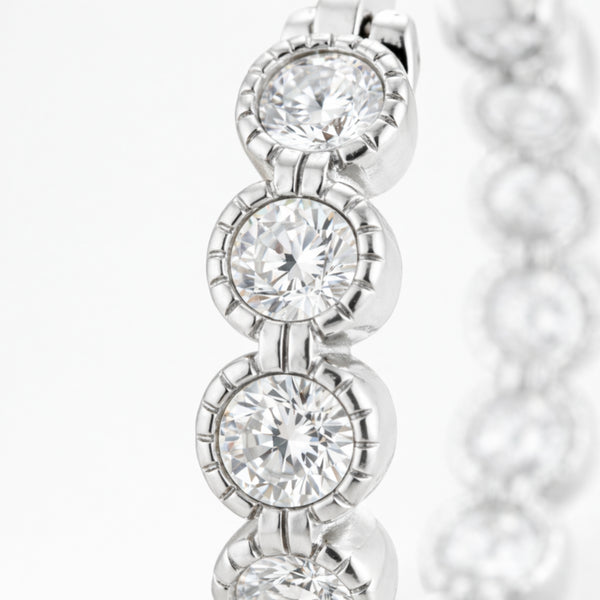 Close up view of silver tone hoop earrings focusing on the round cubic zirconia stones and the detailed polished metal setting.