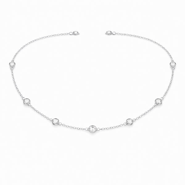 Angled studio view of the silver tone station necklace highlighting the refined chain links and round bezel set stone details.