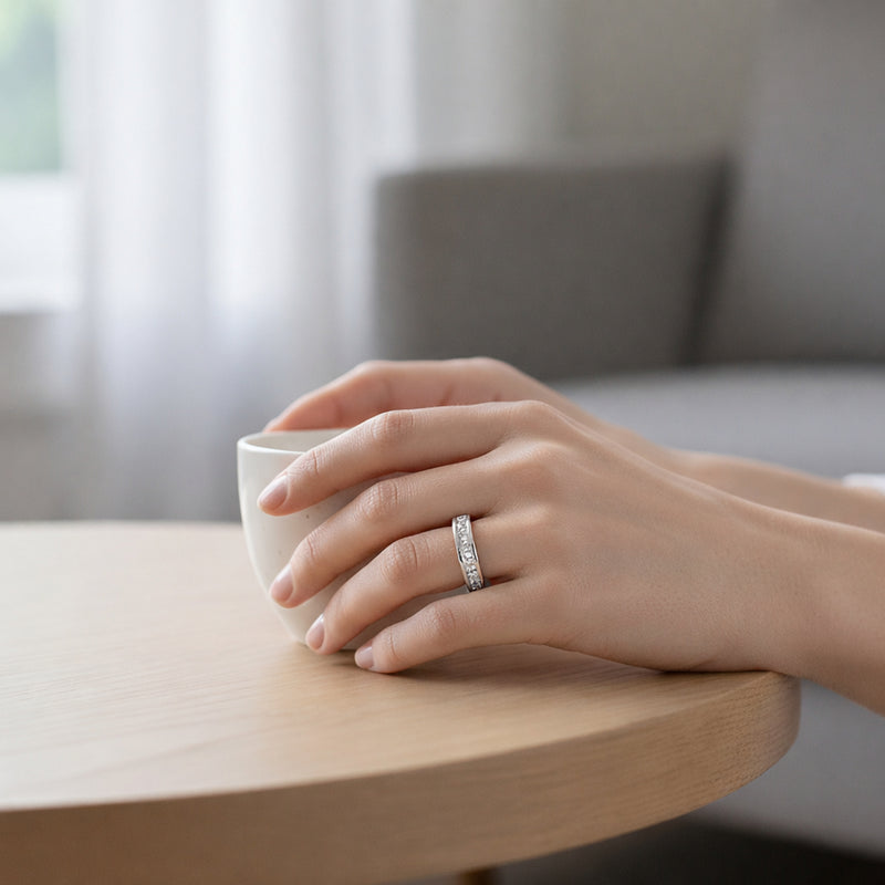 Image shows a Silver Tone band ring worn on a hand while holding a cup. The band features small cubic zirconia stones set along the visible top section.