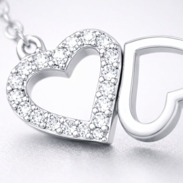 Close up view of the double heart pendant highlighting the pavé set heart and the polished open heart design.