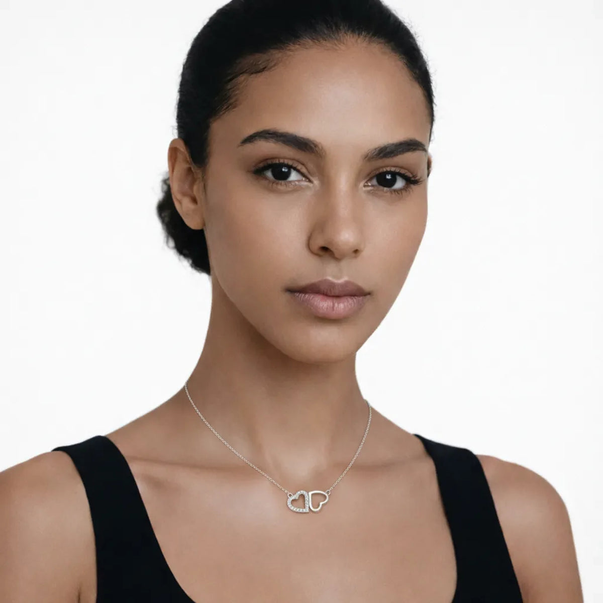 On-model portrait highlights a double heart cubic zirconia pendant, styled with a black scoop-neck top so the pendant stays centered at the neckline.