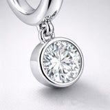 Detail view of the dangling cubic zirconia charm in a smooth bezel style setting attached to a silver tone hoop.