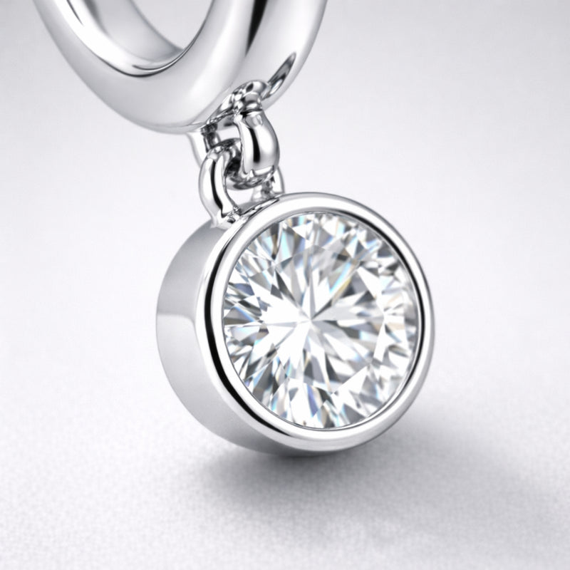 Detail view of the dangling cubic zirconia charm in a smooth bezel style setting attached to a silver tone hoop.