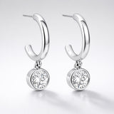 Studio presentation of silver tone hoop earrings with a single round cubic zirconia drop hanging below the hoop.