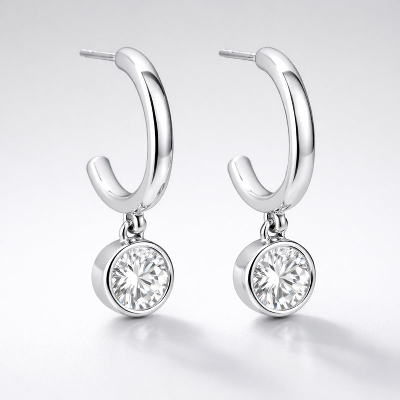 Studio presentation of silver tone hoop earrings with a single round cubic zirconia drop hanging below the hoop.