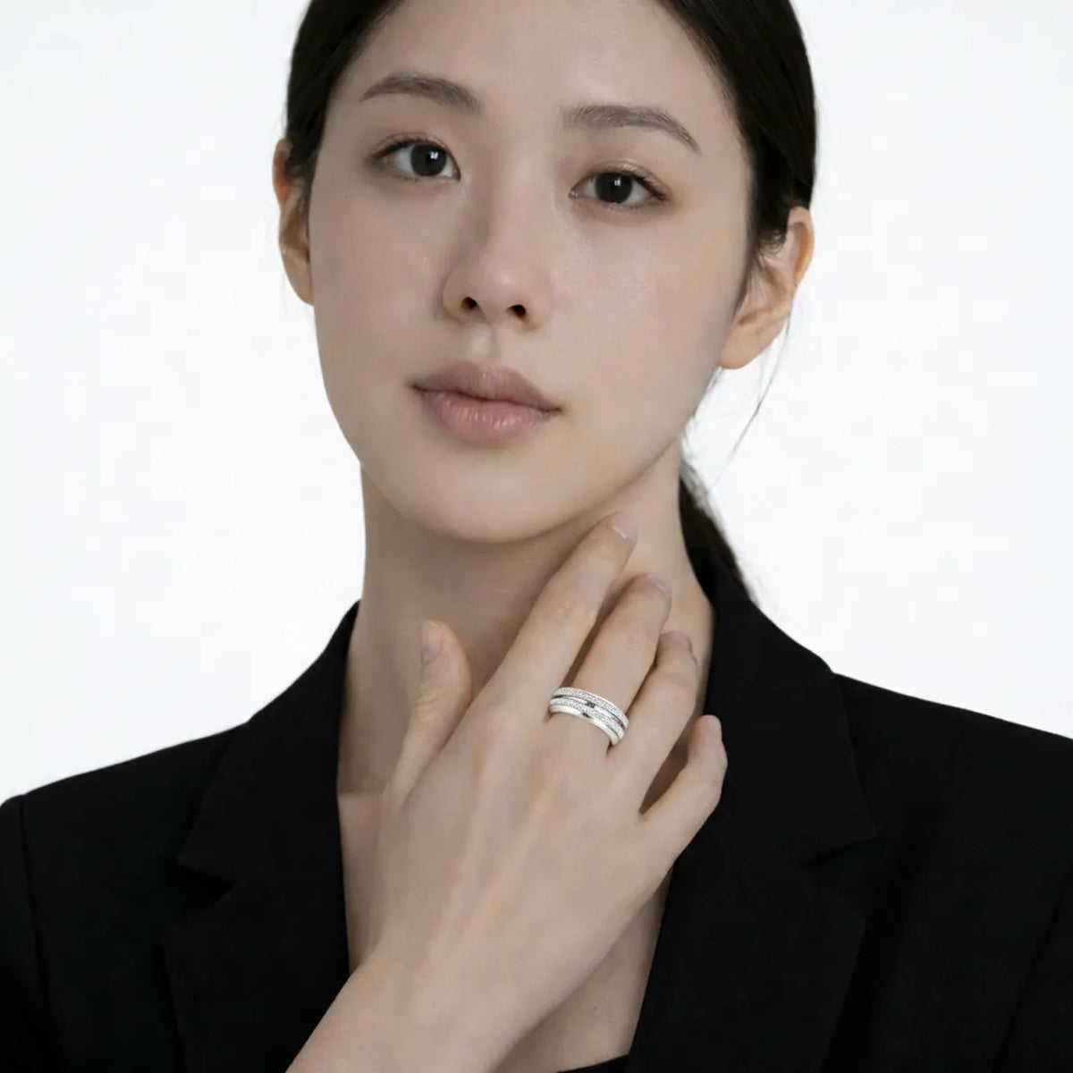 Model shot captures a silver tone intertwined band ring with cubic zirconia, styled with a short-sleeve black dress so the ring sparkles along the fingertips.