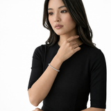 Woman with long dark hair and a black top wearing a silver-tone bracelet, with her hand near her collarbone.