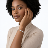 Woman with an afro and beige knit wearing a silver-tone bracelet, with her hand beside her face.