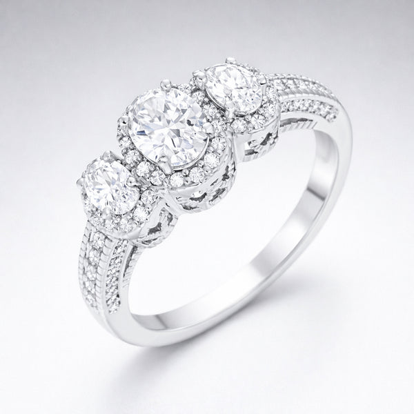 Angled studio view of a three stone halo cubic zirconia ring in silver tone finish, showing the raised settings and pavé accented band.
