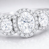 Close up view of a three stone halo cubic zirconia ring in silver tone finish, highlighting the central round stone flanked by two smaller round stones with pavé halos.