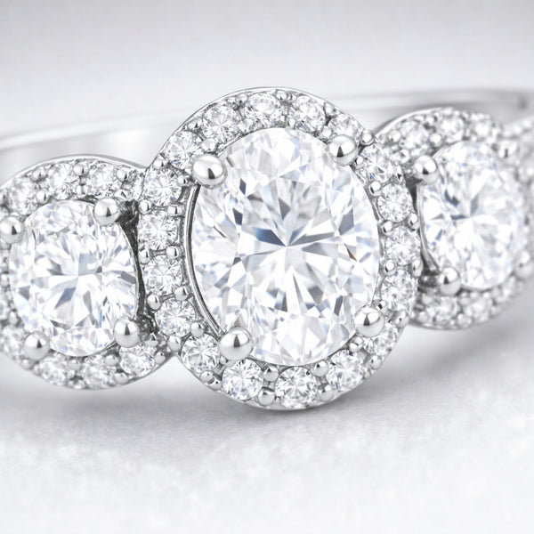 Close up view of a three stone halo cubic zirconia ring in silver tone finish, highlighting the central round stone flanked by two smaller round stones with pavé halos.